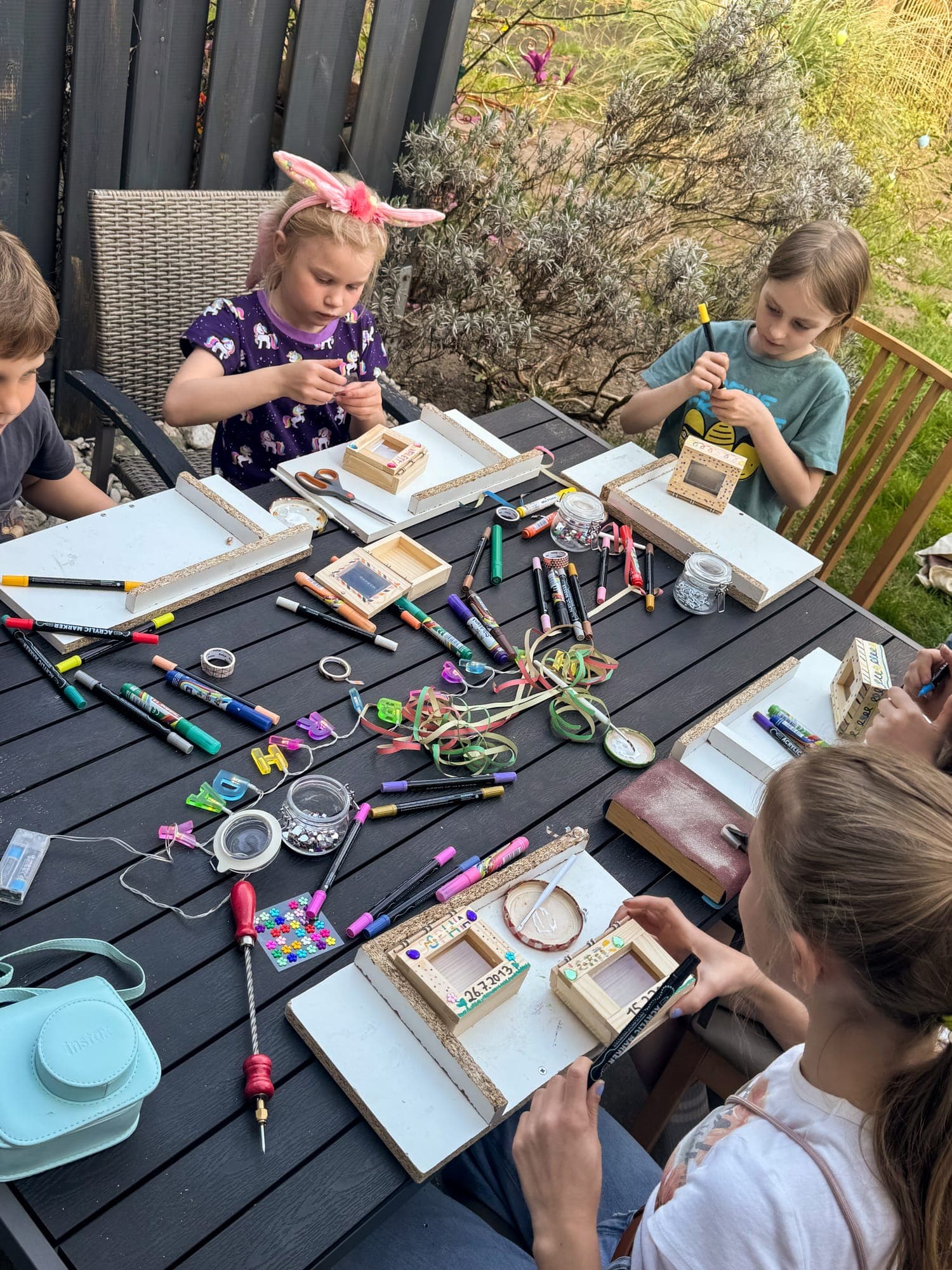 Mehrere Kinder bauen am Gartentisch, eins trägt Hasenohren