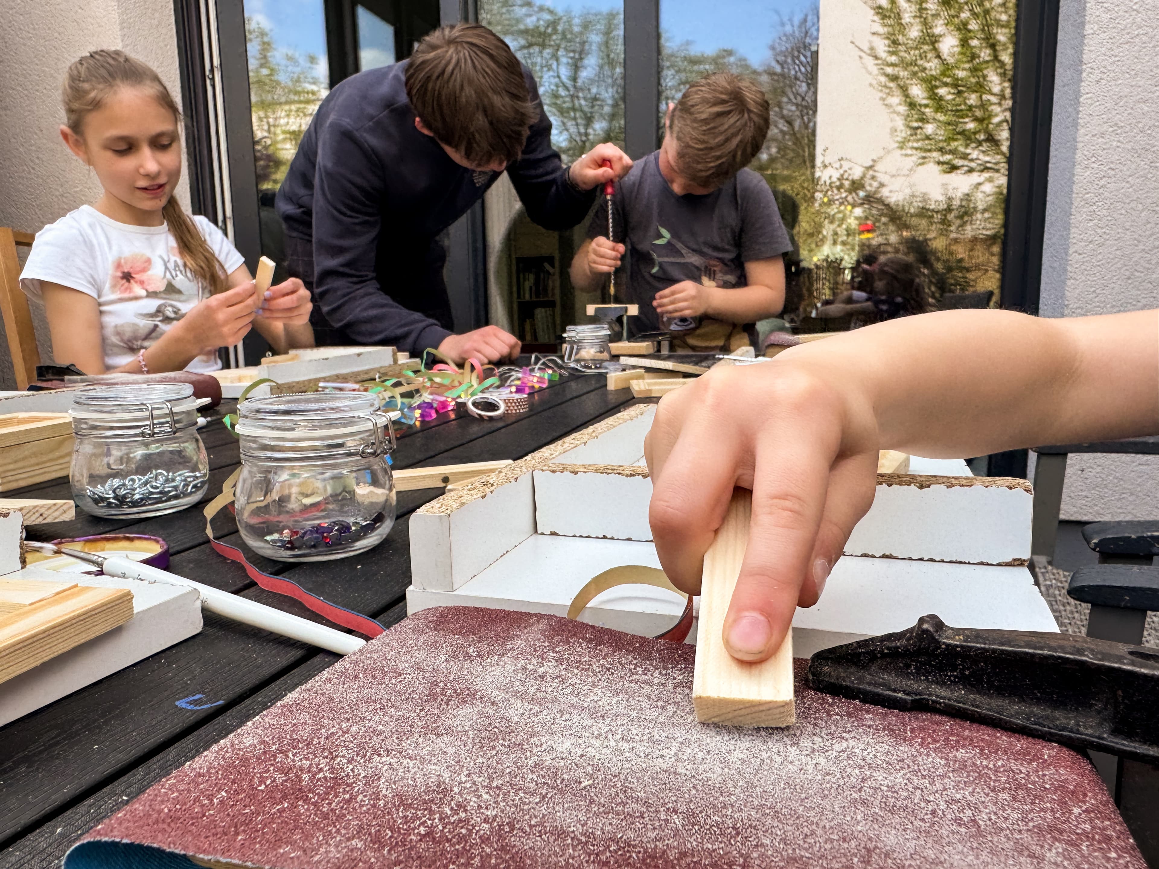 Eine Kinderhand schleift ein Holzstück auf der Schleiffläche der Werkbank