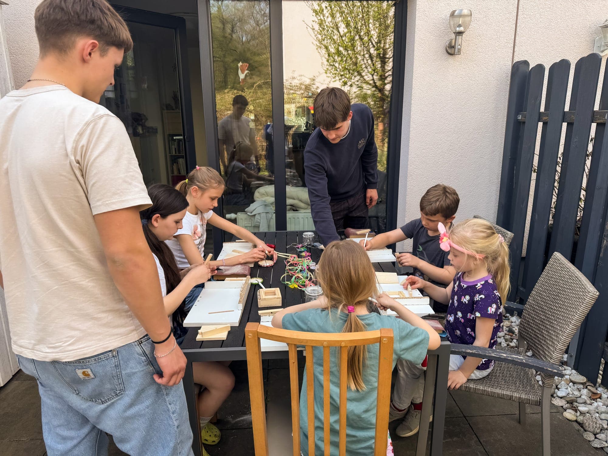 Kinder bauen am Gartentisch, zwei Betreuer helfen ihnen