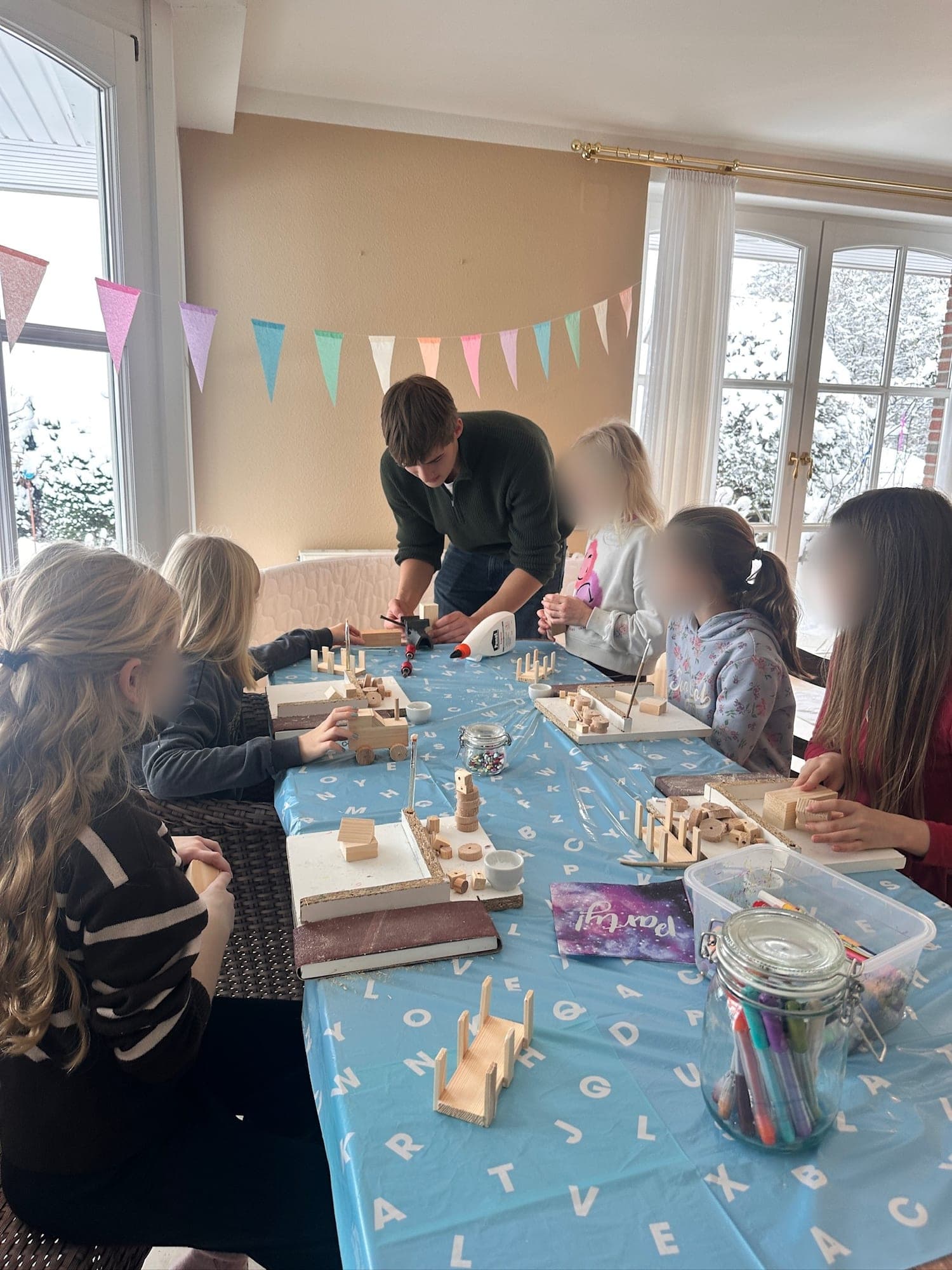 Kindergeburtstag drinnen: Kinder bauen an einem langen Tisch, ein Betreuer hilft